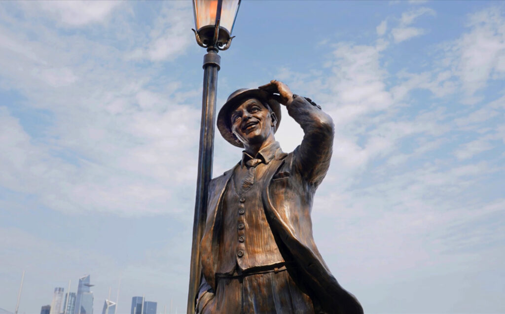 Daytime view of the bronze Frank Sinatra statue shown from below, highlighting the raised arm and lamppost.