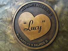 Close-up of a heart-shaped bronze plaque engraved with the name ‘Lucy’.