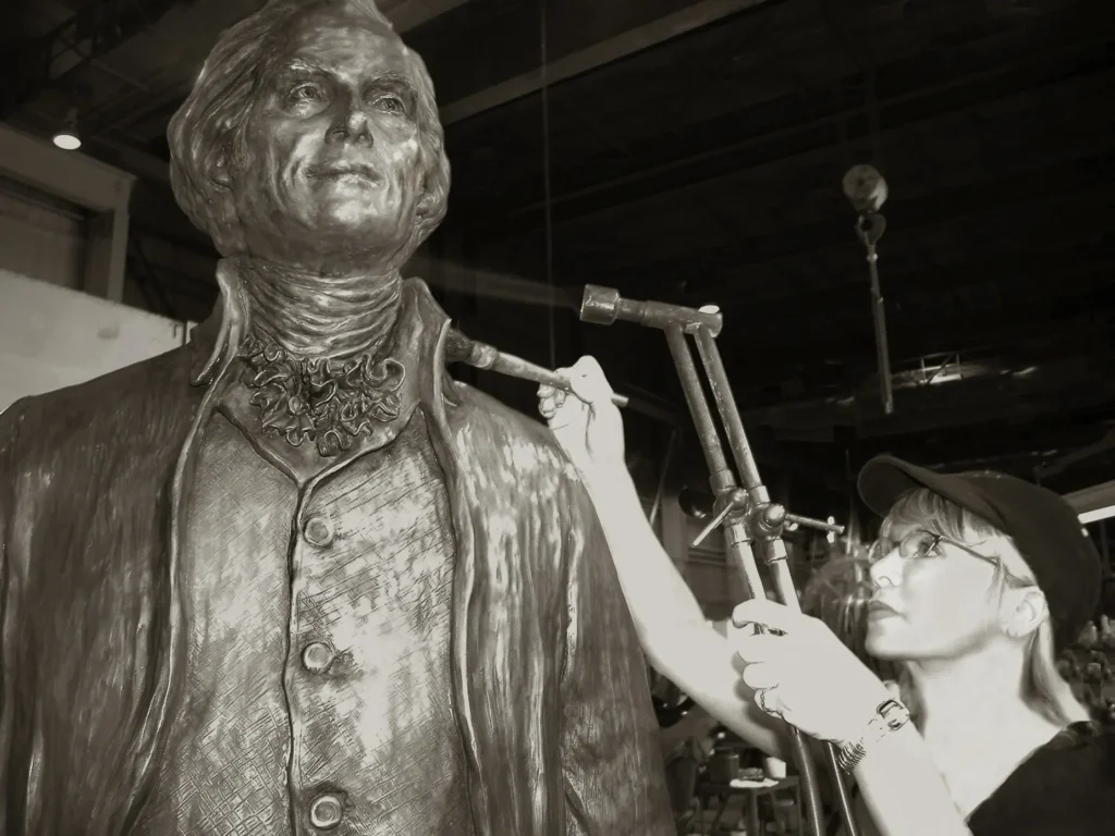 Sculptor working on a clay model of Thomas Jefferson in a studio, using tools to refine the sculpture’s surface.