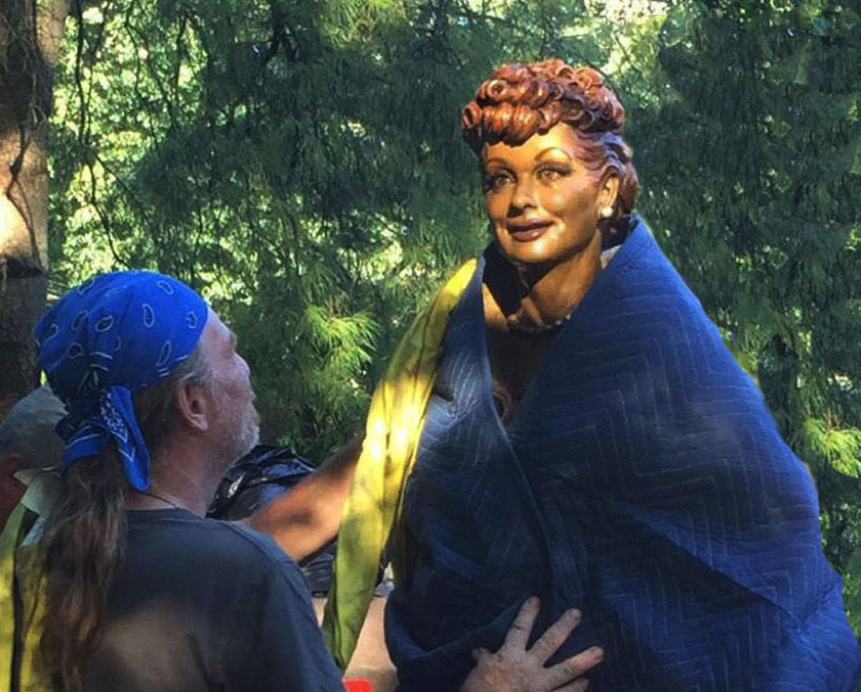 Bronze Lucille Ball statue being positioned during installation, partially wrapped, glowing in early morning sunlight.