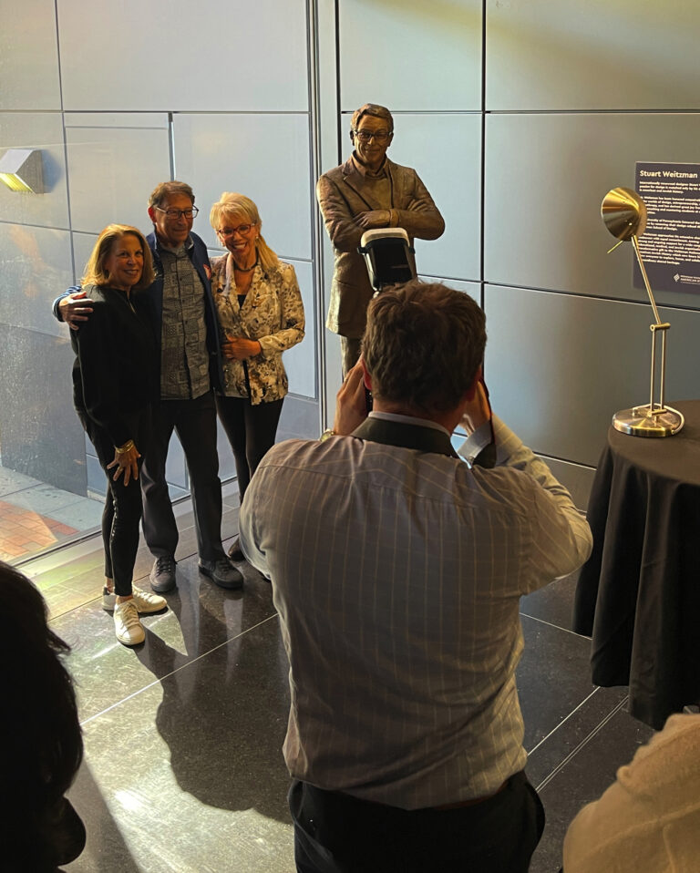 People posing for a photograph in front of the bronze statue of Stuart Weitzman during the unveiling event.