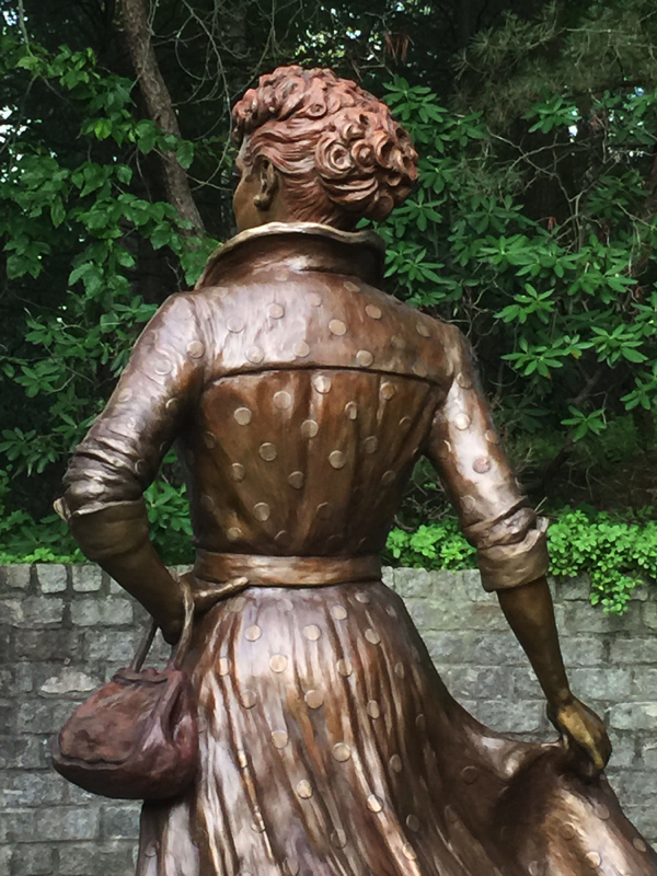 Three-quarter rear view of the bronze Lucille Ball statue, showing the figure turning slightly to the side.