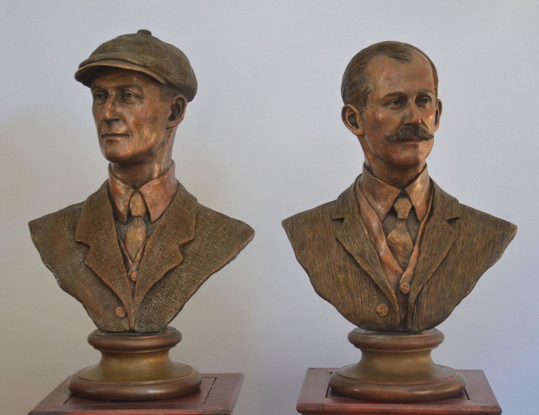Two finished bronze busts of the Wright brothers displayed side by side on pedestals, each wearing early 20th-century attire.