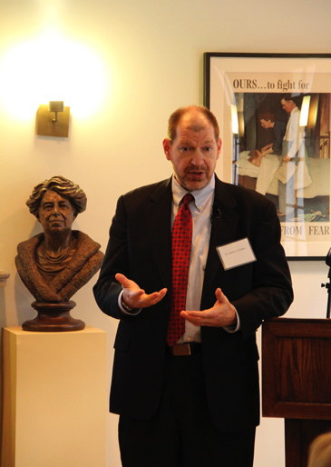 Speaker standing beside a bronze bust of Eleanor Roosevelt during a presentation.