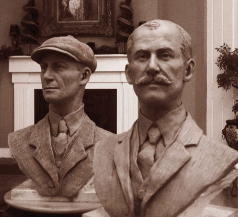 Two sculpted busts of the Wright brothers shown in an earlier material, displayed together indoors before casting in bronze.