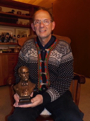 Man seated indoors holding a tabletop bronze bust of Sir William Osler.