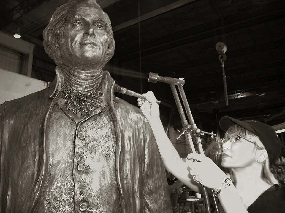 Sculptor working on a clay model of Thomas Jefferson in a studio, using tools to refine the sculpture’s surface.