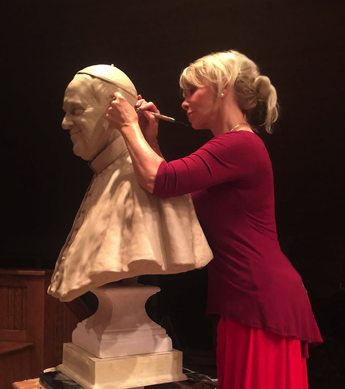 Sculptor Carolyn D. Palmer refining a clay bust of Pope Francis in a studio.