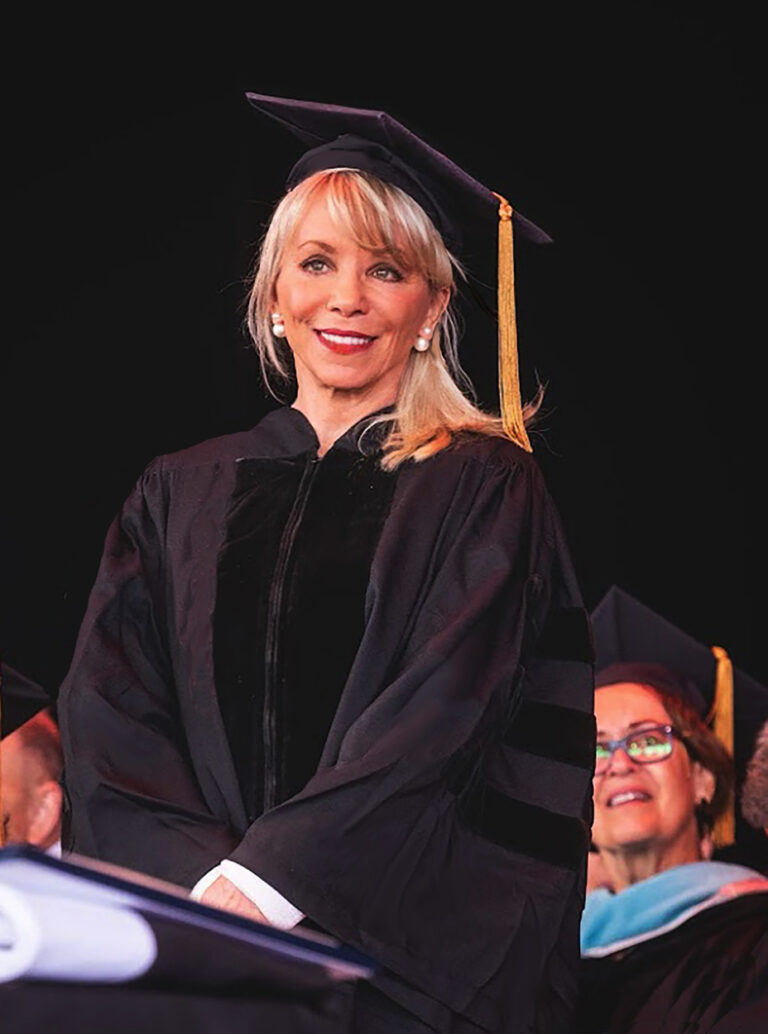 Carolyn D. Palmer standing at a podium in academic regalia during a commencement ceremony.