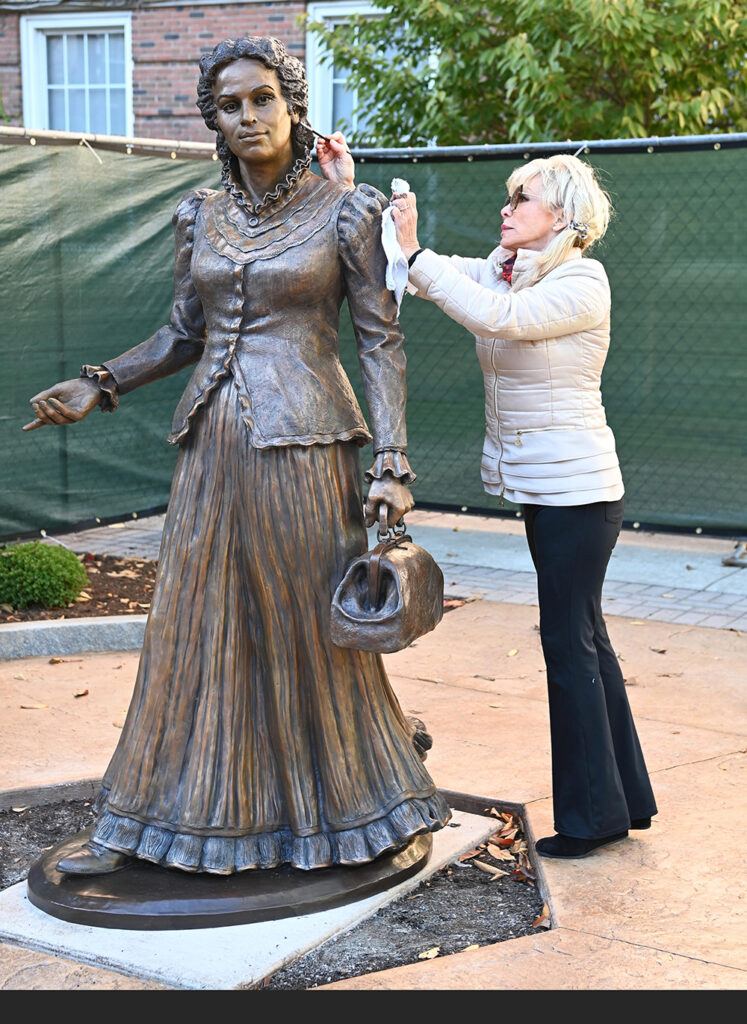 Sculptor Carolyn D. Palmer adjusting details on the bronze statue of Dr. Sarah Loguen Fraser outdoors during installation.