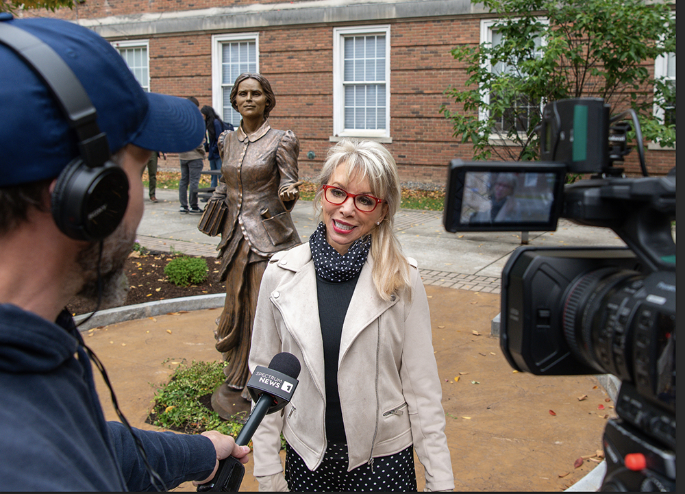Sculptor Carolyn D. Palmer being interviewed on camera beside the bronze statue of Dr. Elizabeth Blackwell.