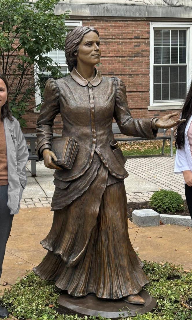 Completed bronze statue of Dr. Elizabeth Blackwell standing outdoors, holding a book and gesturing forward.